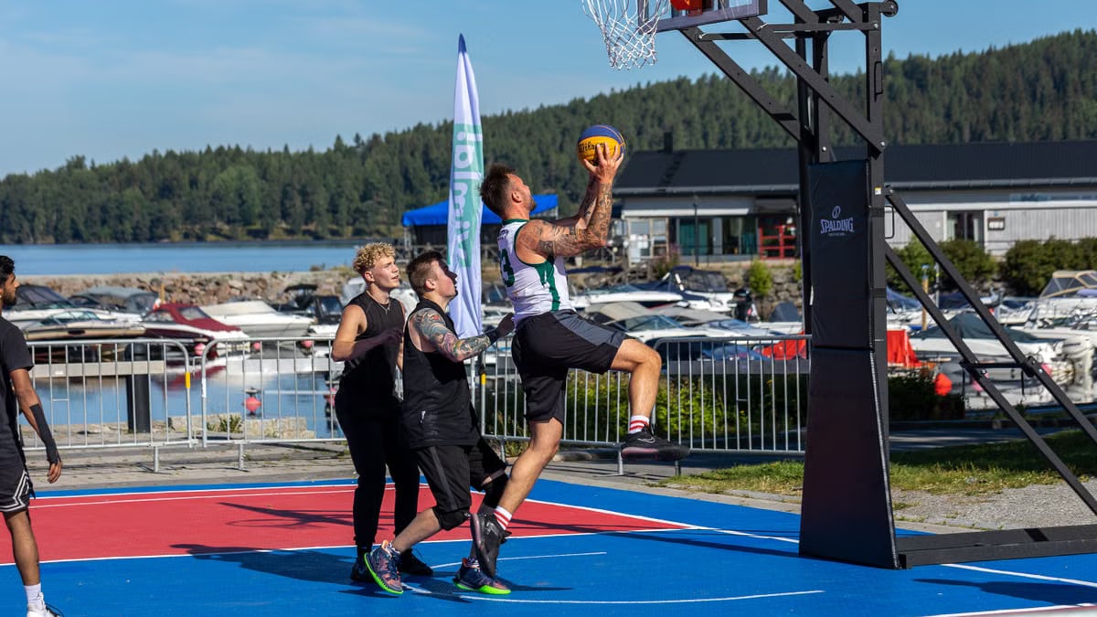 A group of young men playing basketball at an outdoor court near a marina.