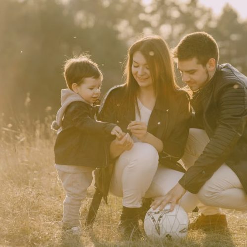 A cheerful family bonding outdoors with a soccer ball, enjoying a sunny day in the grass.