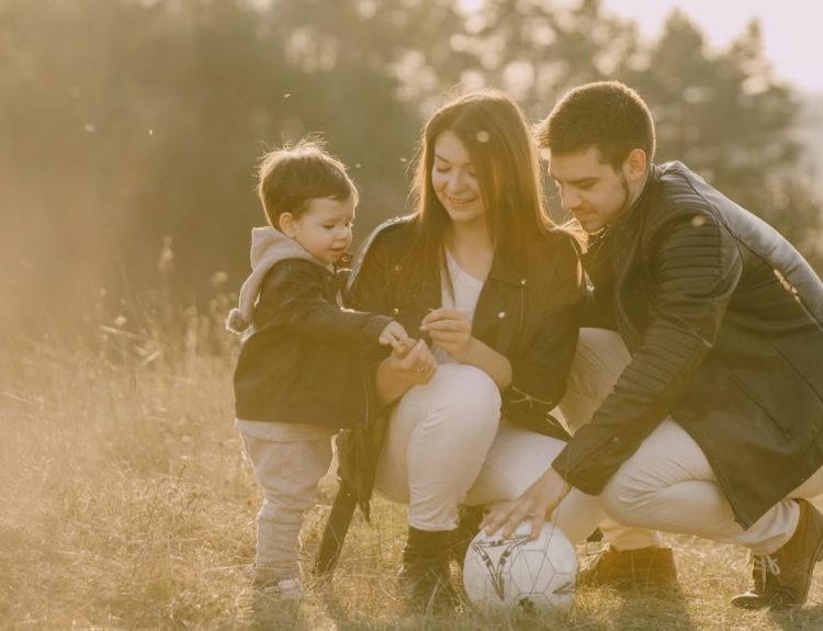 A cheerful family bonding outdoors with a soccer ball, enjoying a sunny day in the grass.