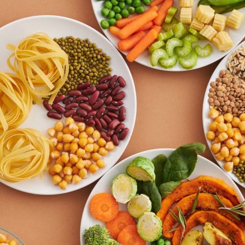A vibrant mix of legumes, vegetables, nuts, and pasta arranged on white plates showcasing a balanced, healthy diet.