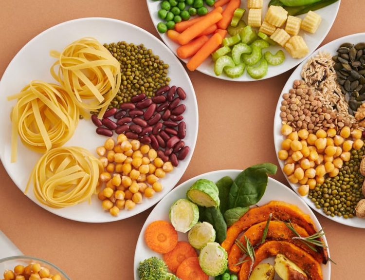 A vibrant mix of legumes, vegetables, nuts, and pasta arranged on white plates showcasing a balanced, healthy diet.