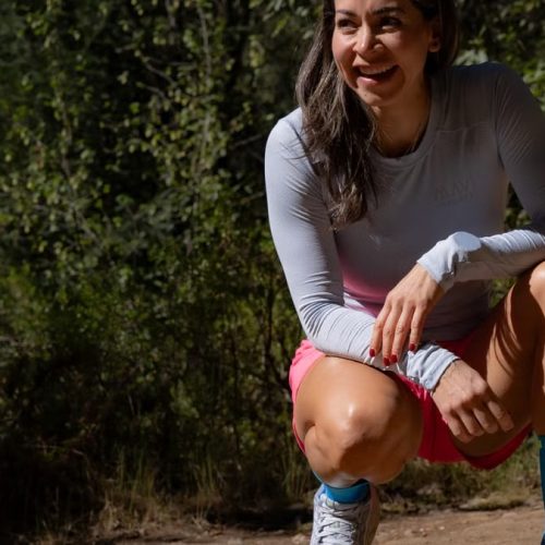 Smiling woman in sportswear takes a break during an outdoor workout, surrounded by nature.