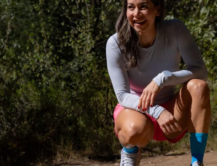 Smiling woman in sportswear takes a break during an outdoor workout, surrounded by nature.